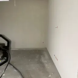 Wnętrze pokoju w trakcie przygotowania do prac wykończeniowych w Barlinku. Widoczne ściany po szpachlowaniu, jeszcze przed malowaniem, z wystającymi przewodami elektrycznymi oraz fragmentem...