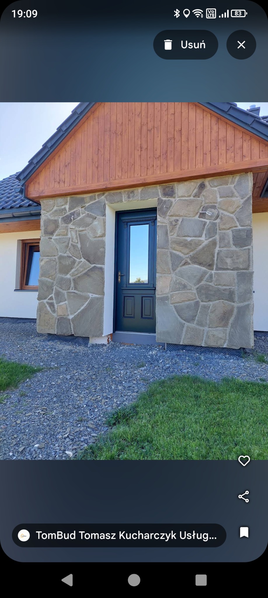 Wejście do domu w Żywcu z kamienną elewacją i ciemnymi drzwiami. Widoczne drewniane elementy wykończeniowe i fragment trawnika. Ujęcie z poziomu gruntu.