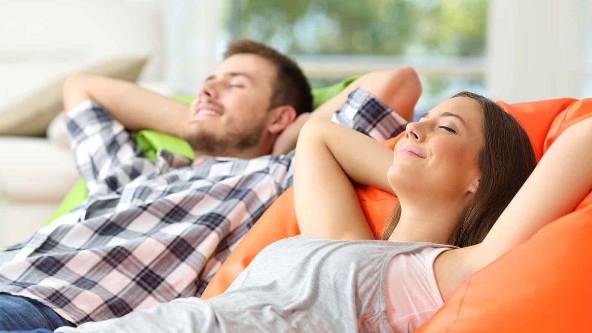 Para relaksuje się na kolorowych pufach w jasnym wnętrzu, z zamkniętymi oczami i uśmiechem na twarzy, sugerując komfort i odprężenie.