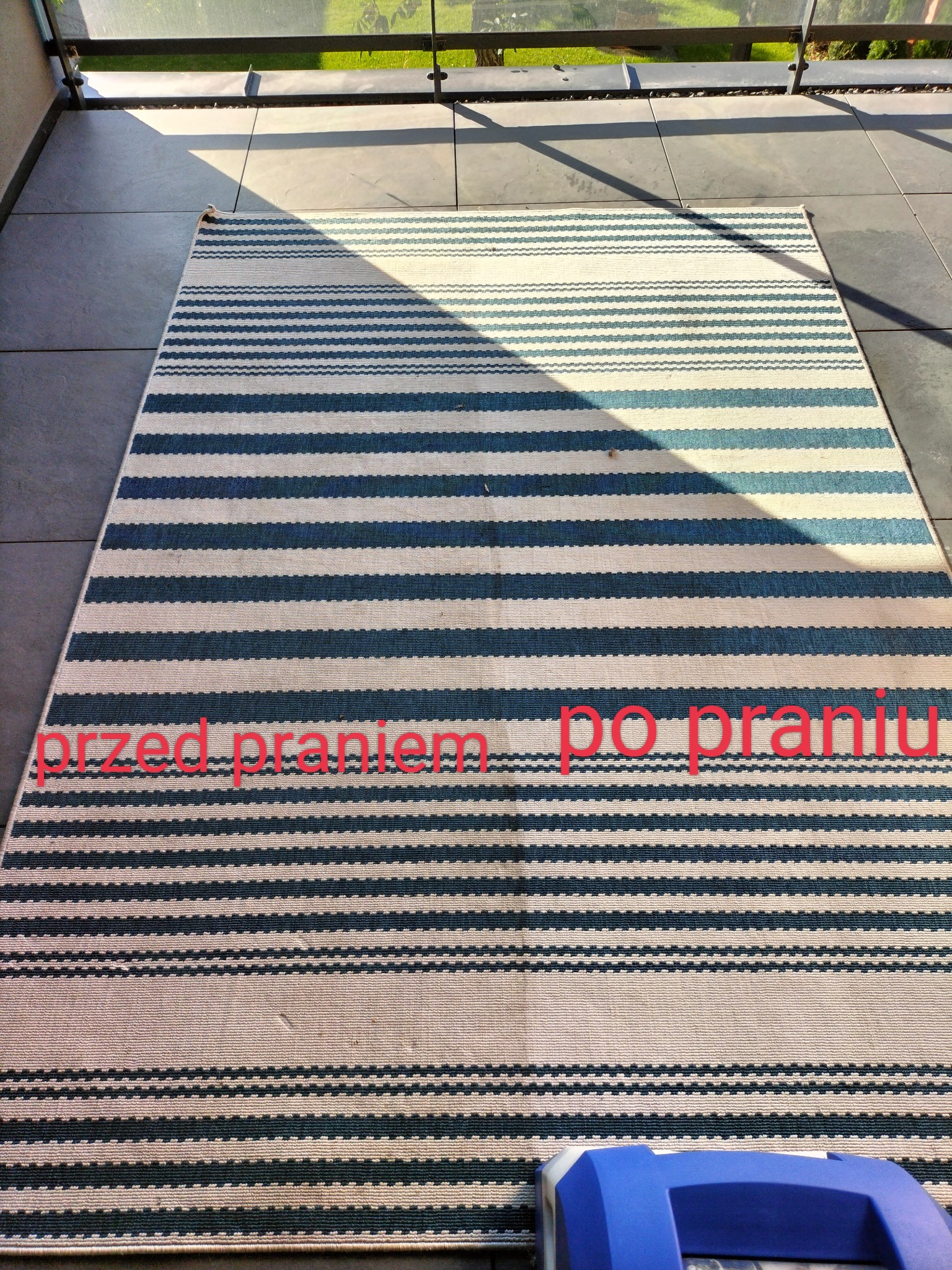 Pasiasty dywan na balkonie z tekstem 'przed praniem' i 'po praniu' naniesionym na zdjęcie, dolna krawędź częściowo zasłonięta przez niebieskie urządzenie czyszczące.
