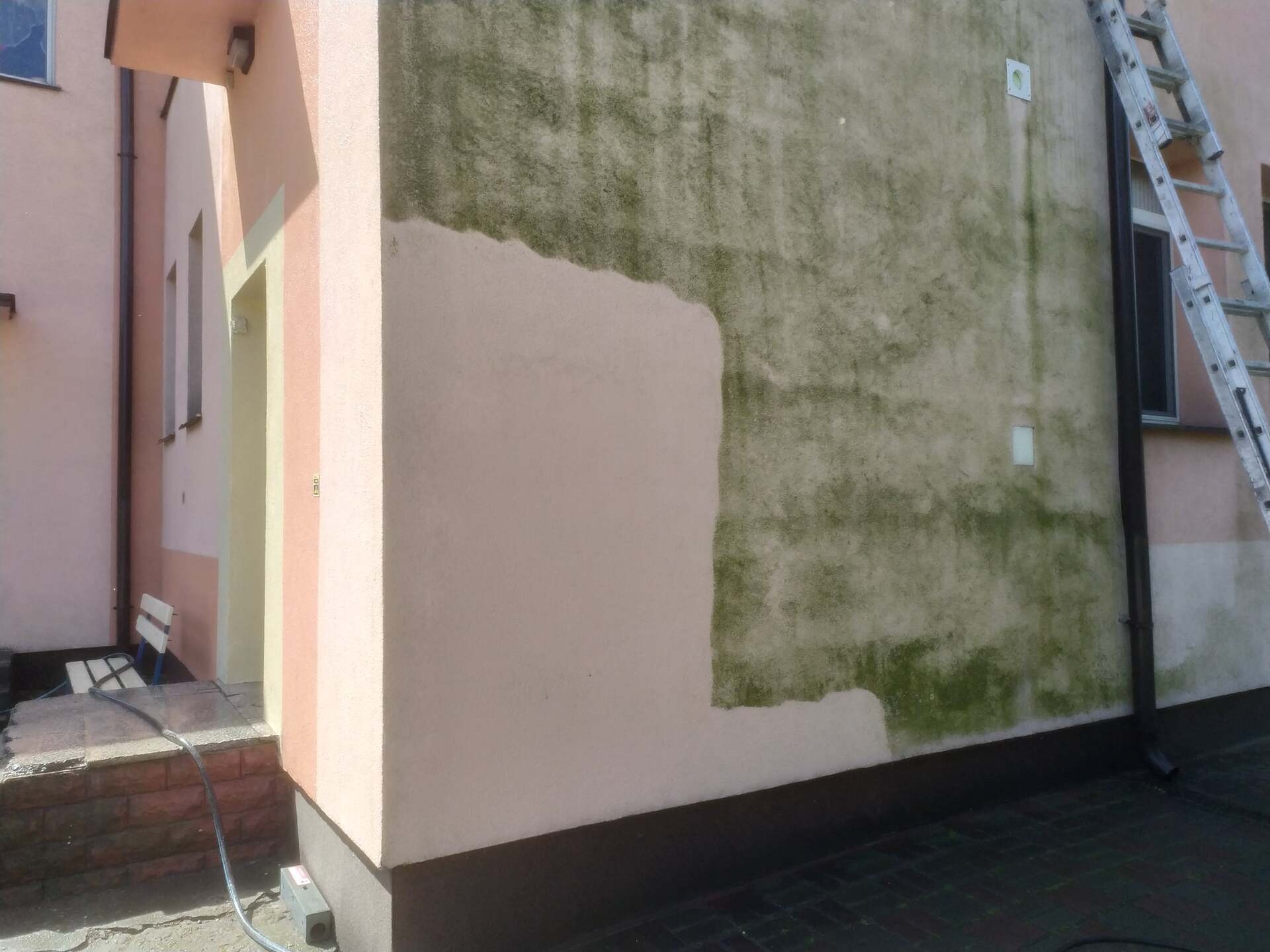 Fragment ściany budynku przed i po czyszczeniu z zielonego nalotu. Widoczna drabina i sprzęt do mycia ciśnieniowego.