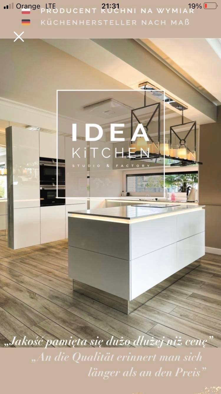 Wnętrze nowoczesnej kuchni z białą wyspą kuchenną, oświetleniem LED i błyszczącymi frontami, prezentowane jako realizacja firmy 'Idea Kitchen Studio & Factory'.