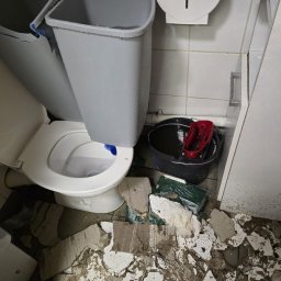 SERWIS JACEK MARTA PIECZONKA - Zniszczona toaleta z pękniętą muszlą, gruzem na podłodze, wiadrem z brudną wodą i narzędziami, ukazująca stan po awarii hydraulicznej.