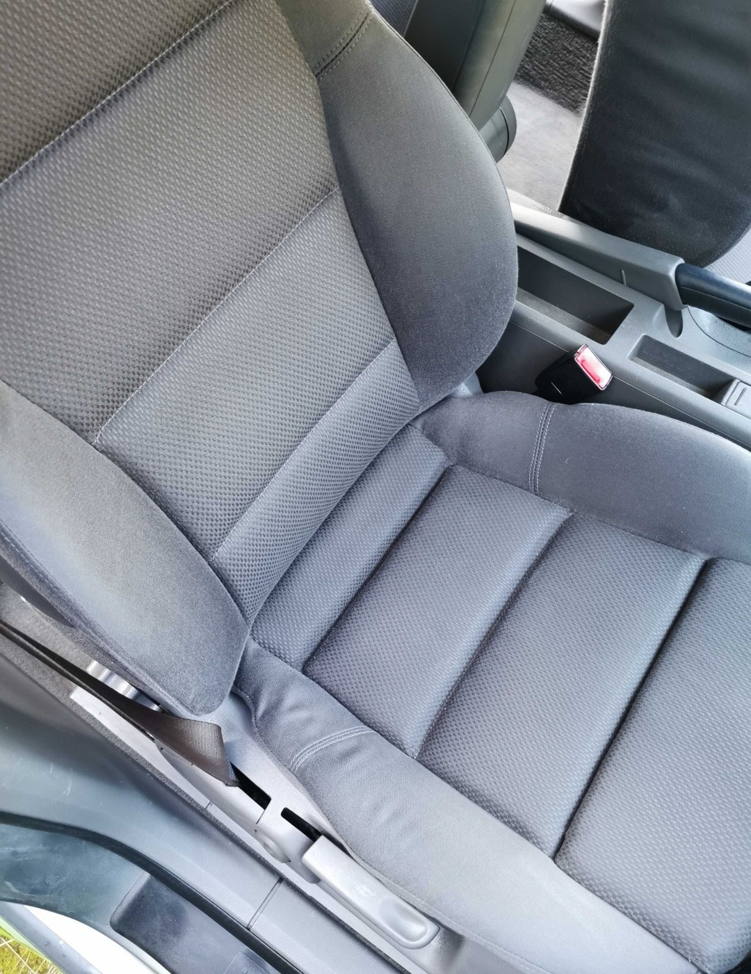 Szare, teksturowane siedzenie samochodowe z widocznym pasem bezpieczeństwa i elementami regulacji.