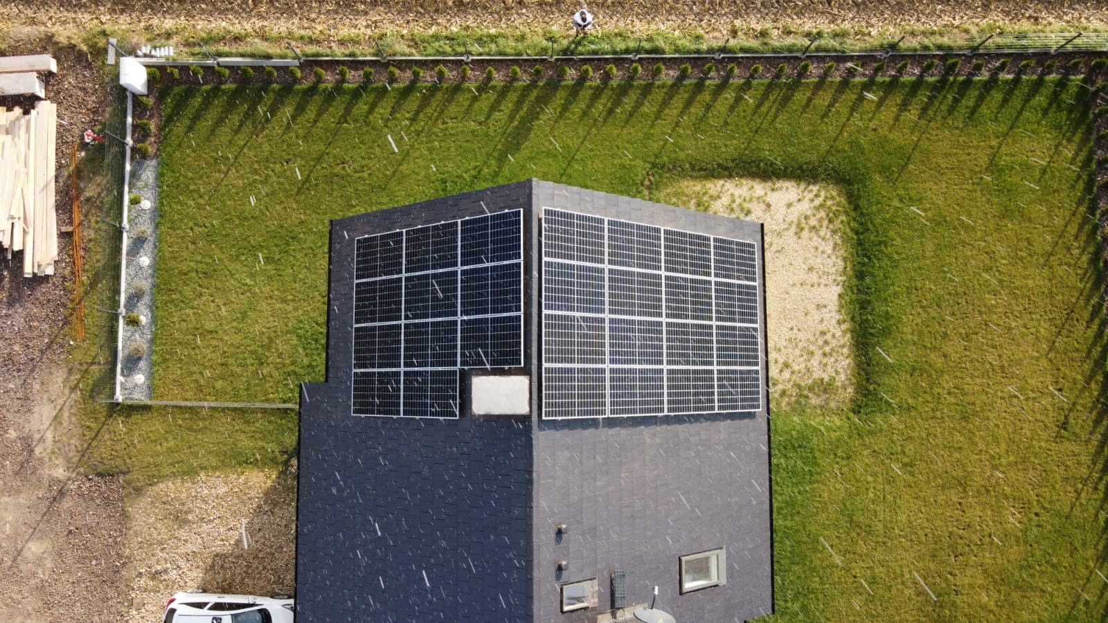 Widok z góry na dom z panelami słonecznymi na dachu, obok zadbany trawnik i częściowo widoczny samochód dostawczy