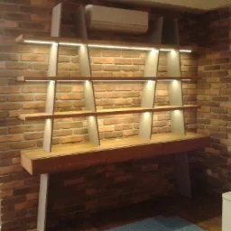 Regał na wymiar z drewnianymi p&oacute;łkami i oświetleniem LED wbudowanym w p&oacute;łki, na tle ściany z czerwonej cegły.