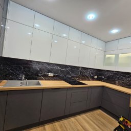 A.M.G. KATOWICE SPÓŁKA Z OGRANICZONĄ ODPOWIEDZIALNOŚCIĄ - Nowoczesna kuchnia z szarymi szafkami dolnymi, białymi górnymi i blatem z drewnopodobnego laminatu. Czarny panel ścienny z białym marmurkowym wzorem.