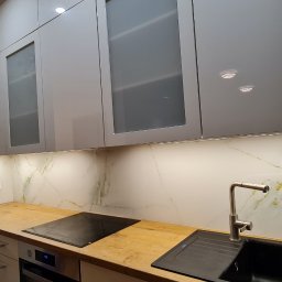 A.M.G. KATOWICE SPÓŁKA Z OGRANICZONĄ ODPOWIEDZIALNOŚCIĄ - Nowoczesna kuchnia z szarymi szafkami, drewnianym blatem i marmurowym panelem ściennym z złotymi żyłkami. Oświetlenie LED pod szafkami górnymi.