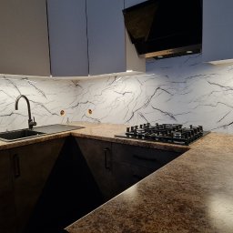 A.M.G. KATOWICE SPÓŁKA Z OGRANICZONĄ ODPOWIEDZIALNOŚCIĄ - Nowoczesna kuchnia z marmurowym panelem szklanym nad blatem, oświetleniem LED i czarną armaturą. Widoczne gniazdka elektryczne i płyta gazowa.