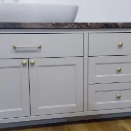 Szara szafka łazienkowa pod umywalkę z blatem imitującym marmur i złotymi gałkami, widok z bliska.