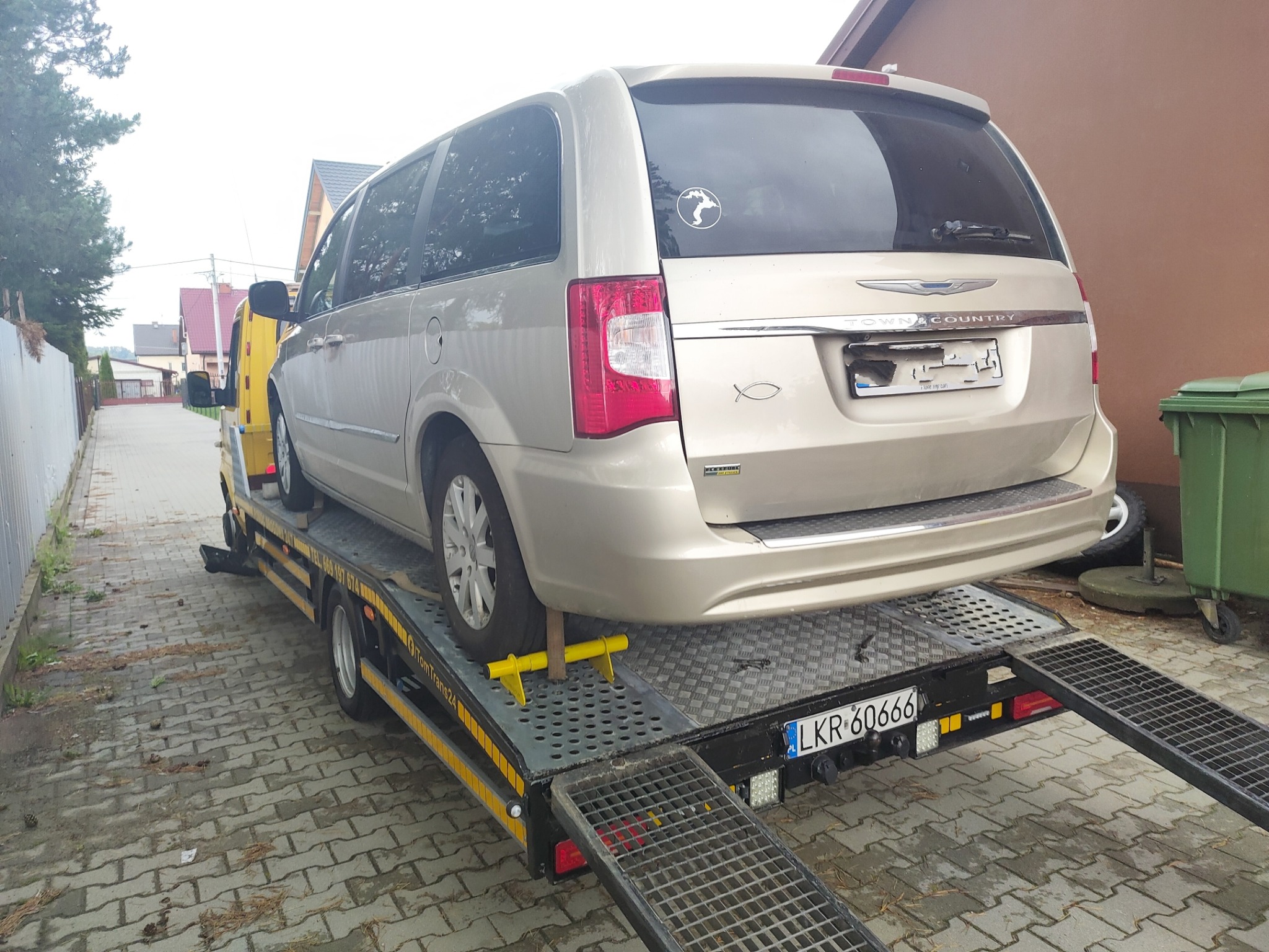 Złoty minivan Chrysler Town & Country zabezpieczony na platformie lawety z żółtymi blokadami kół, widok z tyłu, tablica rejestracyjna LKR 60666.