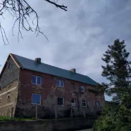 Dwukondygnacyjny budynek z nowym, zielonym dachem, widoczny z dołu, z elementami drzew w kadrze.