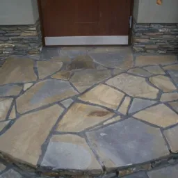 Kamienny chodnik z nieregularnych płyt prowadzący do drzwi wejściowych w Nowym Sączu, wykończony kamienną okładziną.