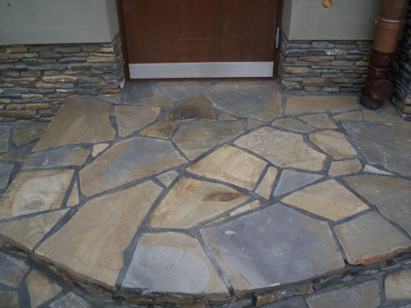 Kamienny chodnik z nieregularnych płyt prowadzący do drzwi wejściowych w Nowym Sączu, wykończony kamienną okładziną.