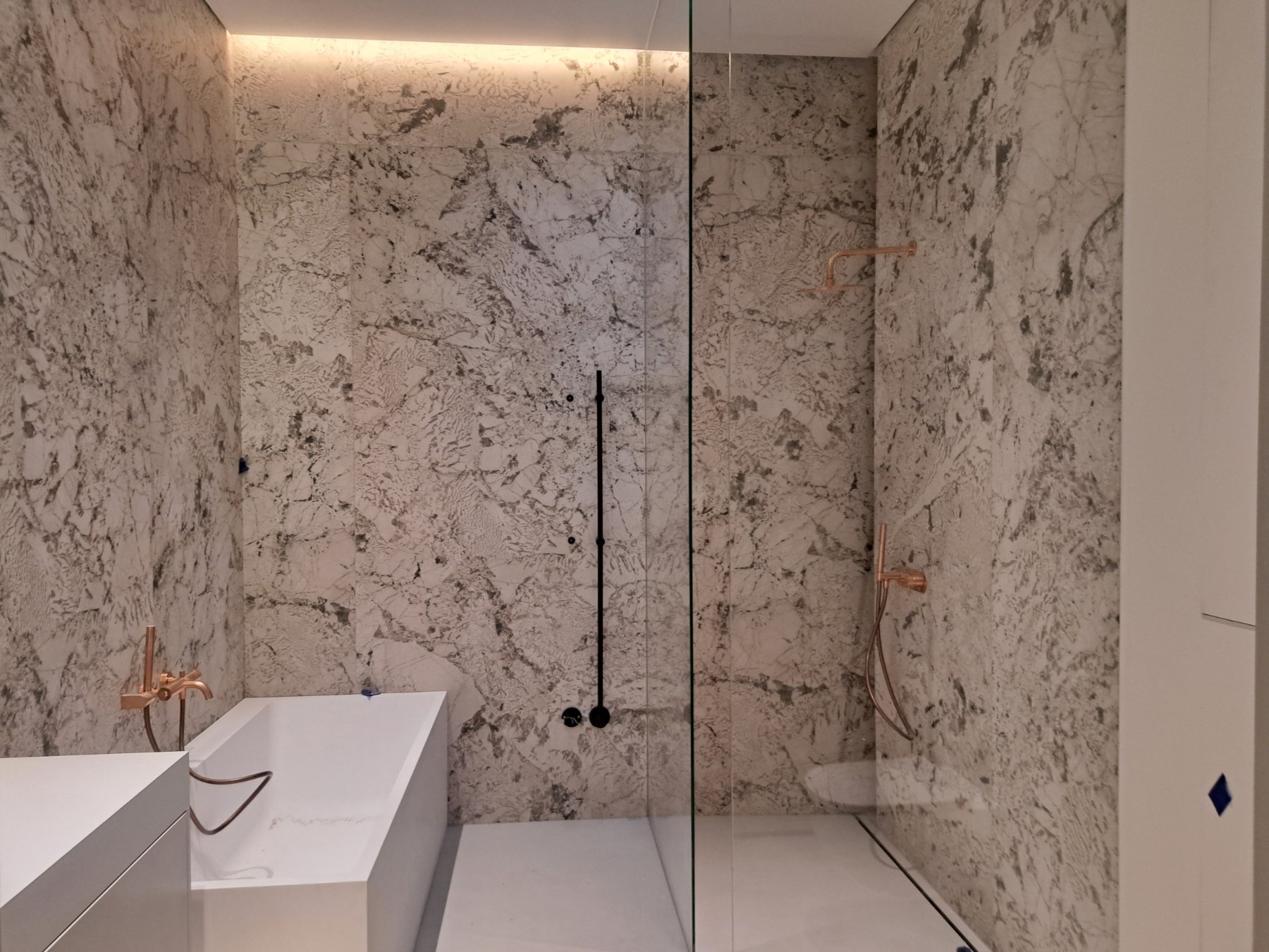 Nowoczesna łazienka z marmurowymi ścianami, szklaną kabiną prysznicową i armaturą w kolorze różowego złota.