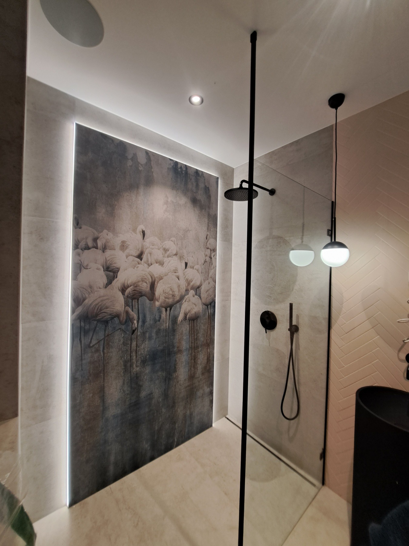 Nowoczesna łazienka z kabiną prysznicową typu walk-in, czarną armaturą, podświetlanym obrazem z motywem flamingów i ścianą wykończoną w jodełkę.