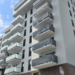 Grzegorz Kowalczyk GLOBAL-BUD - Nowoczesny budynek wielorodzinny z białymi ścianami i balkonami z szarymi balustradami. Ujęcie z dołu, widoczne błękitne niebo. Minimalistyczna architektura.