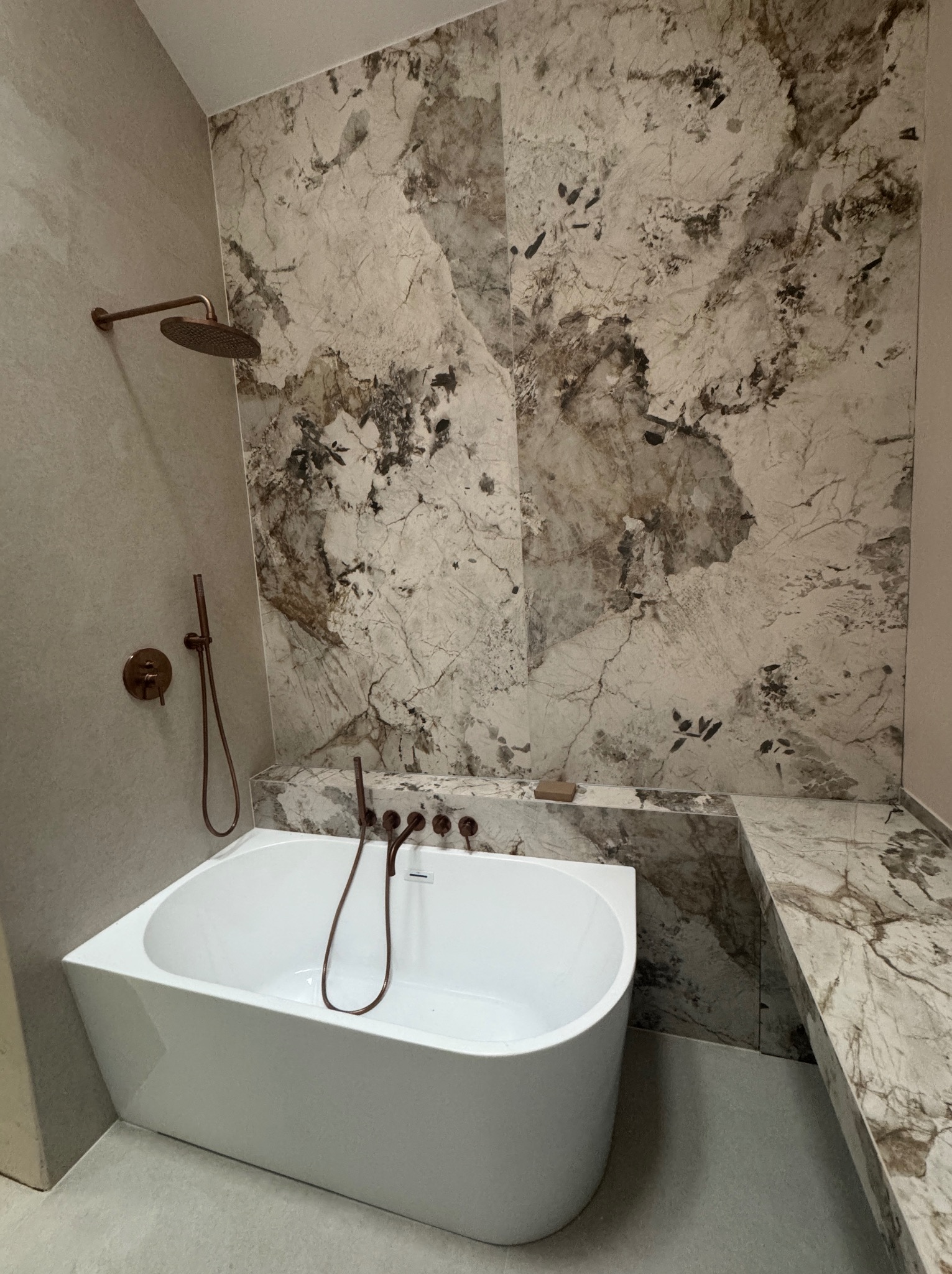 Nowoczesna łazienka z białą wanną, marmurową ścianą i armaturą w kolorze miedzi. Minimalistyczny design z akcentem luksusu i elegancji. Wykończenie z dbałością o detale.