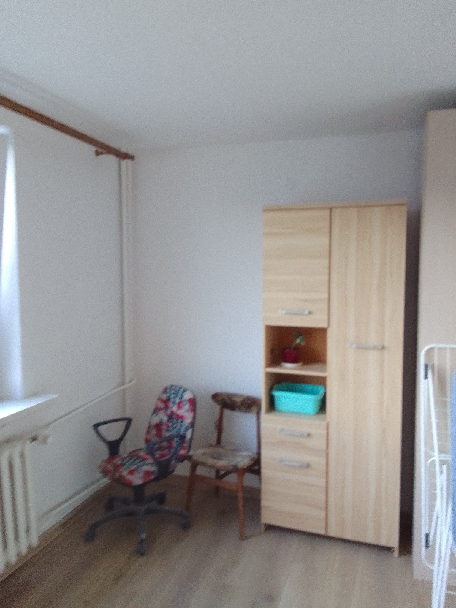 Pusty pokój z drewnianą podłogą, szafą z jasnego drewna, biurkiem i krzesłami, przygotowany do odświeżenia ścian