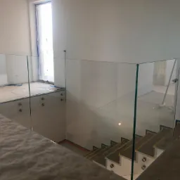 Szklana balustrada zamontowana na schodach i antresoli w trakcie wykańczania wnętrza w Choczewie, widoczne mocowania punktowe.