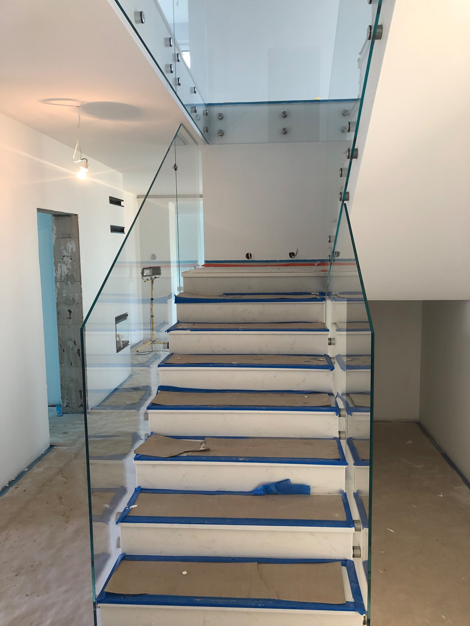 Szklana balustrada schodowa w trakcie montażu, zabezpieczone stopnie, widoczne mocowania punktowe.