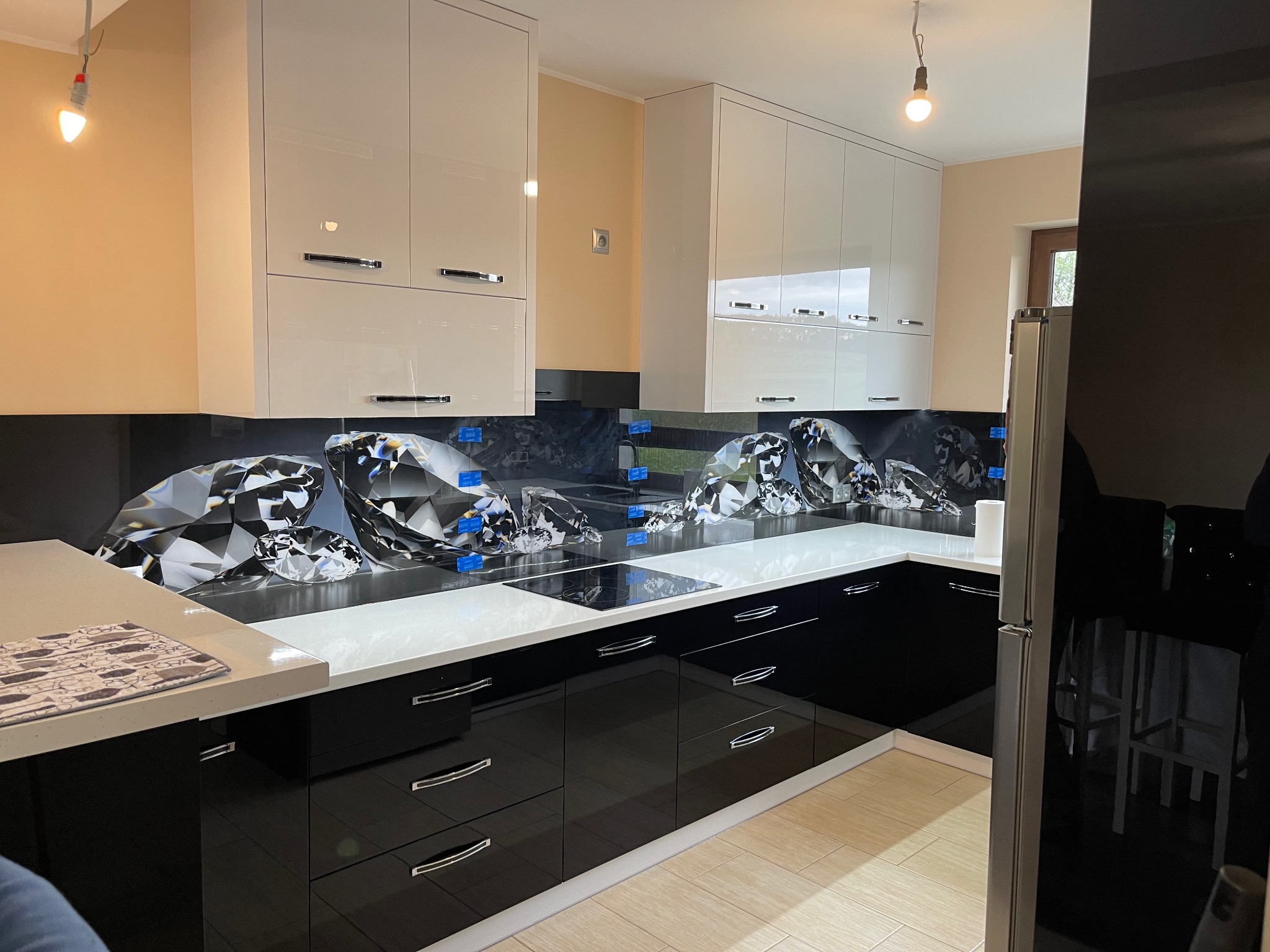Nowoczesna kuchnia z czarnymi szafkami i białym blatem, ozdobiona panelem szklanym z motywem diamentów na ścianie nad blatem.