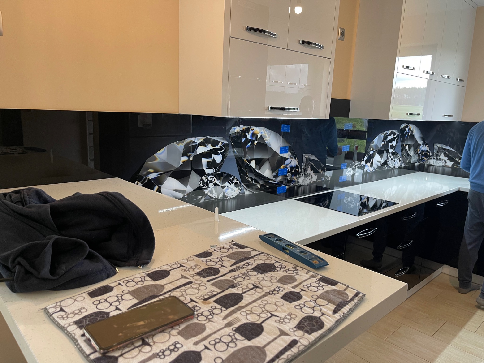 Szklany panel dekoracyjny z motywem diamentów w kuchni, widoczny poziomica i czarna bluza na blacie.