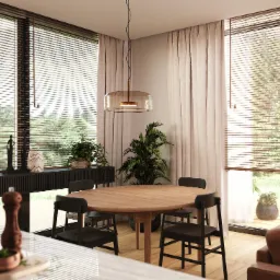 Jasne wnętrze jadalni z okrągłym drewnianym stołem, czarnymi krzesłami, komodą z dekoracjami i roślinami, oświetlone wiszącą lampą z kloszem z przydymionego szkła, widok na zieleń za oknem...