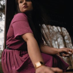 MAUPACYKA.PL Marcin Klinikowski - Kobieta w fioletowej sukience w kropki siedzi w altanie, spoglądając w lewo, z widocznym złotym zegarkiem i pierścionkiem na palcu.