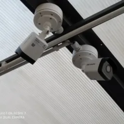 Dwie białe kamery monitoringu marki Hikvision zamontowane pod transparentnym zadaszeniem z widocznymi elementami mocującymi.