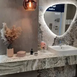 Nowoczesna łazienka z marmurowym blatem, owalnym lustrem z podświetleniem LED, wiszącymi lampami kulistymi i dekoracyjnym bukietem w wazonie.