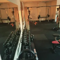 Siłownia: stojaki z hantlami, ławeczki do ćwiczeń, suwnice Smitha i lustra w tle.