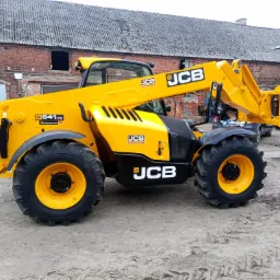 Żółta ładowarka teleskopowa JCB 541-70 Interhandler na placu budowy z ceglanym budynkiem w tle.