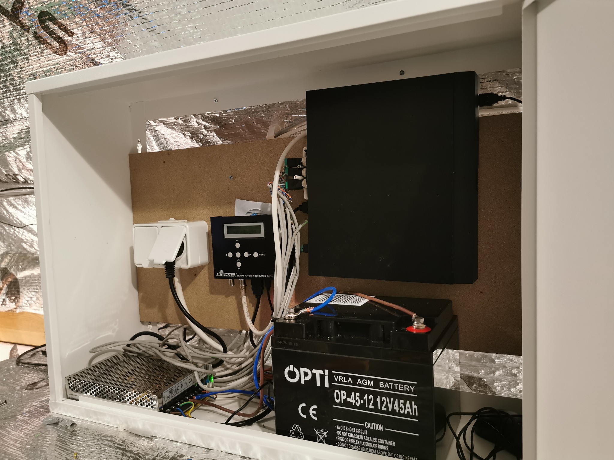 Wnętrze szafki z zamontowanym akumulatorem OPTI VRLA AGM 12V45Ah, modułem SIGNAL-420 DVB-T, zasilaczem impulsowym oraz okablowaniem, całość umieszczona w obudowie z izolacją termiczną.
