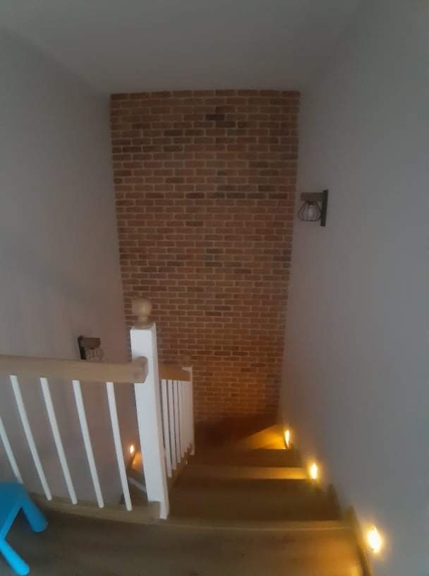 Klatka schodowa z oświetleniem punktowym na stopniach i ścianą z cegły klinkierowej, widok z góry, białe balustrady.