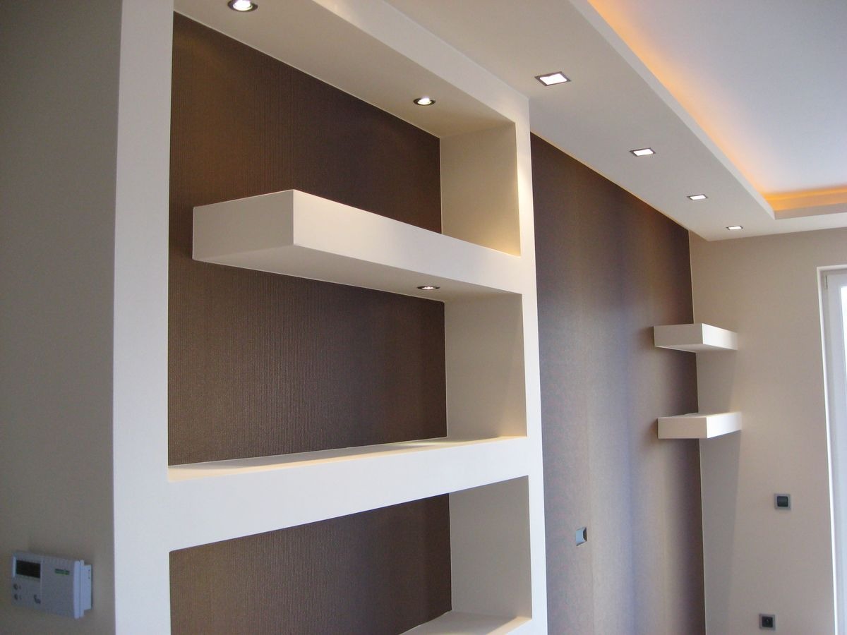 Nowoczesne wnętrze z brązową ścianą, białymi półkami w zabudowie i oświetleniem punktowym LED w suficie podwieszanym. Widoczny fragment ściany z termostatem.