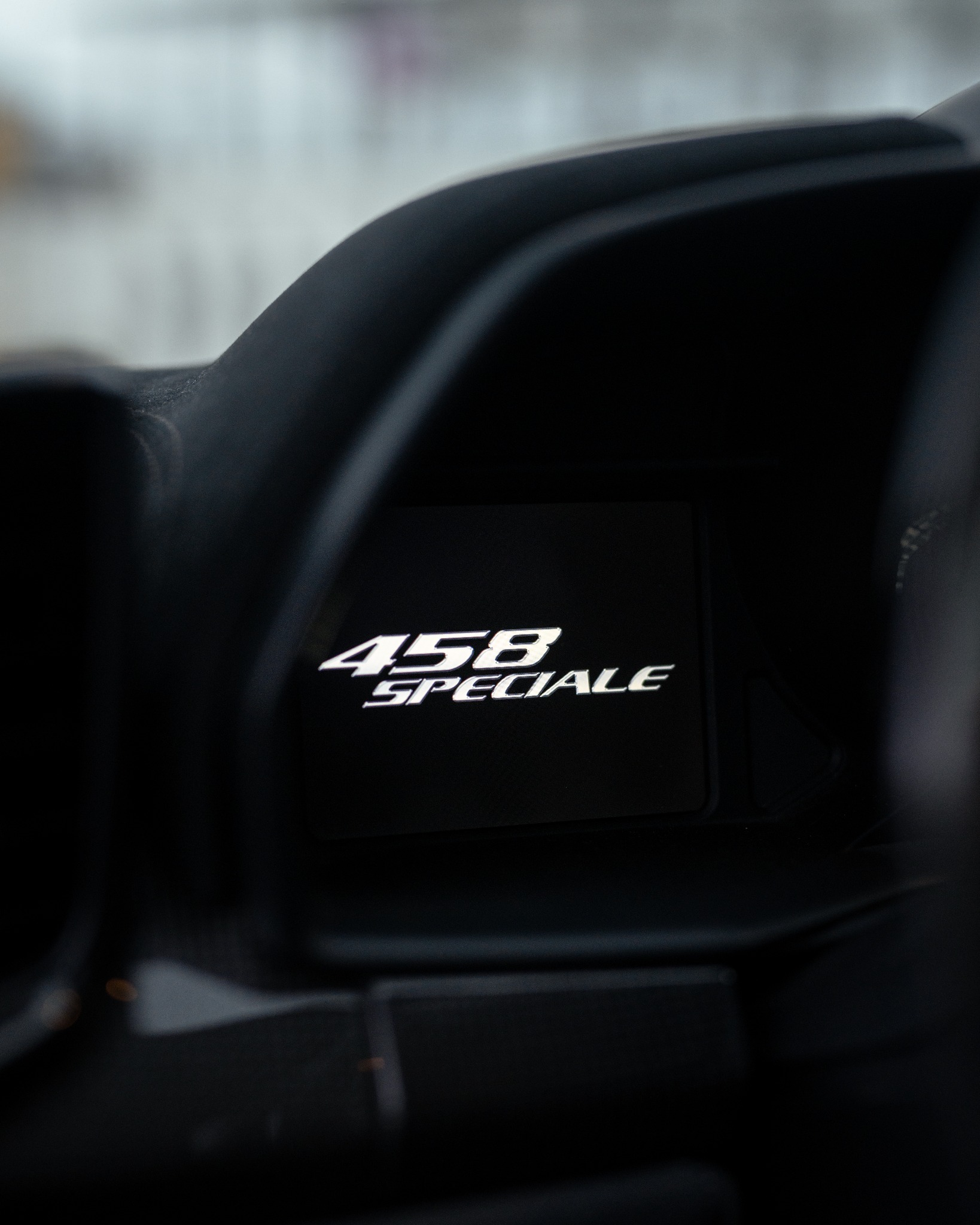 Szczegółowe ujęcie podświetlanego napisu '458 SPECIALE' na czarnym elemencie wnętrza samochodu, z delikatnym rozmyciem tła.