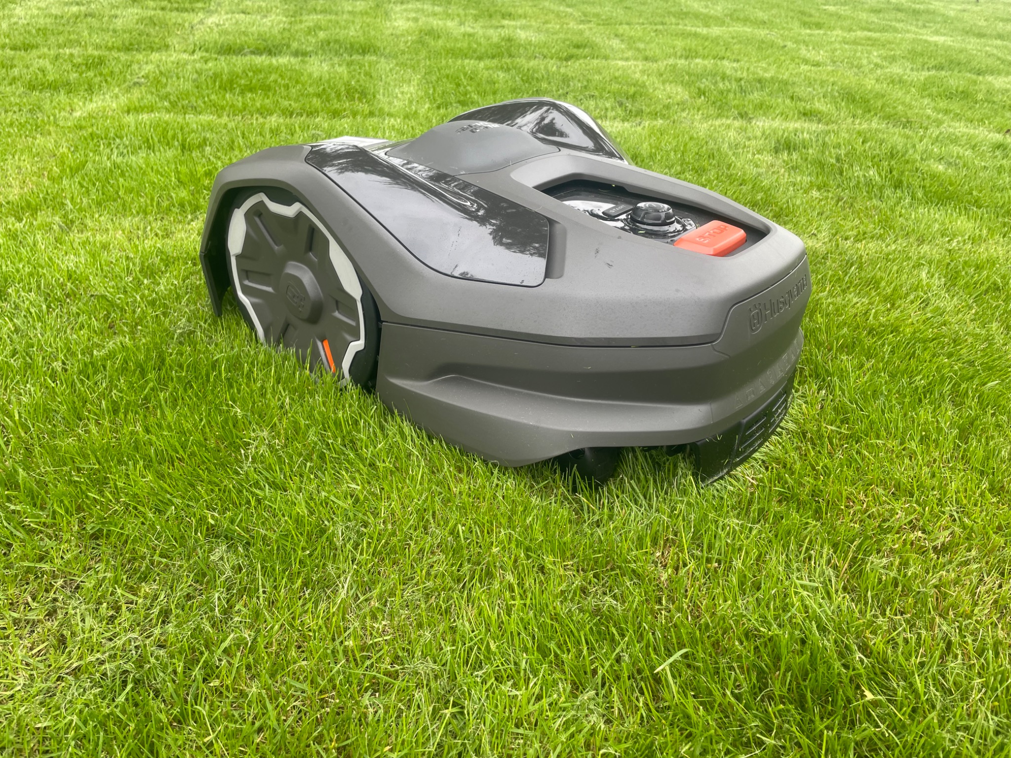 Szary, automatyczny robot koszący Husqvarna na zielonym, równo przystrzyżonym trawniku w słoneczny dzień. Widoczne ślady po koszeniu.