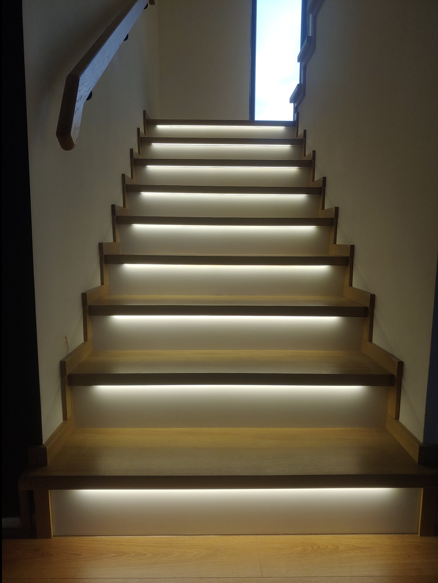 Schody drewniane z podświetleniem LED pod każdym stopniem, widok od dołu, jasne oświetlenie, nowoczesny design.