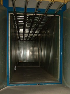 Wnętrze kabiny lakierniczej z systemem transportu podwieszanego, widok od wejścia, ściany metalowe, oświetlenie górne.