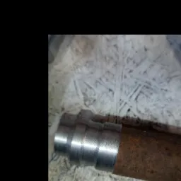 Fragment rury z nałożonym metalowym pierścieniem z widocznymi śladami obróbki na tle płyty OSB.