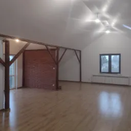 Przestronne, jasne poddasze po remoncie z drewnianą konstrukcją nośną, wykończone cegłą, z oknem dachowym i panelami podłogowymi w odcieniach brązu.