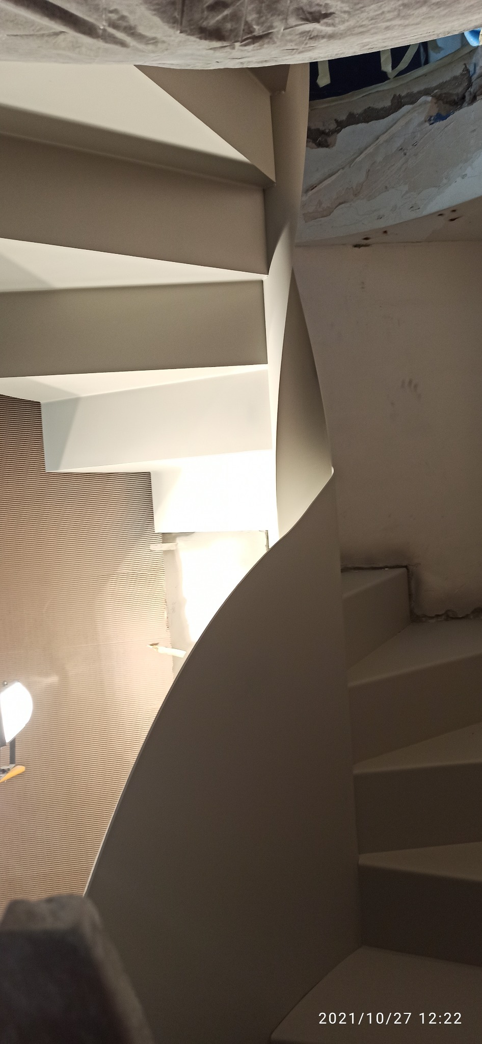 Klatka schodowa spiralna w trakcie wykończenia w Dąbrowie Górniczej, widoczne ślady po remoncie i oświetlenie robocze.