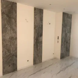 Wnętrze pokoju z ułożonymi płytkami imitującymi marmur na podłodze i fragmentach ścian, widoczne otwory na gniazdka elektryczne i wyprowadzone przewody oświetleniowe.