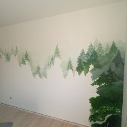 LukZar - Ściana z ręcznie malowanym motywem leśnym, imitującym mglisty krajobraz z zielonymi drzewami iglastymi. Widoczne narzędzia malarskie.