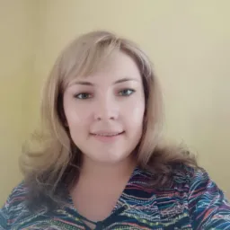 Portret uśmiechniętej kobiety z blond włosami i w bluzce z kolorowym wzorem na żółtym tle.