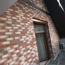 Good Value - Ceglana elewacja budynku z oknem, widoczny fragment dachu i klimatyzator na zewnątrz.