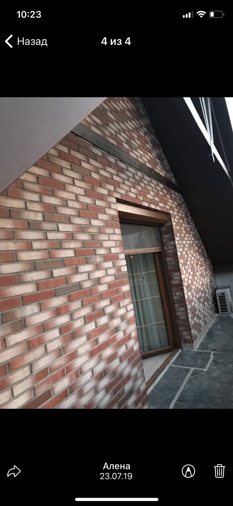 Ceglana elewacja budynku z oknem, widoczny fragment dachu i klimatyzator na zewnątrz.