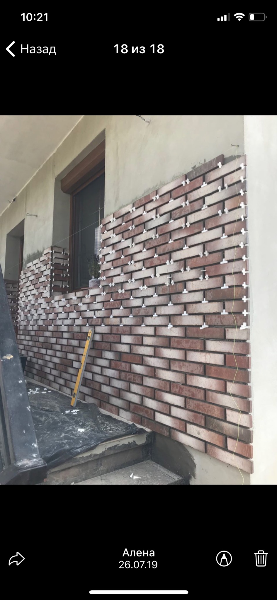 Montaż cegieł klinkierowych na elewacji budynku z użyciem krzyżyków dystansowych, widoczny poziomica i częściowo zakryte folią podłoże.