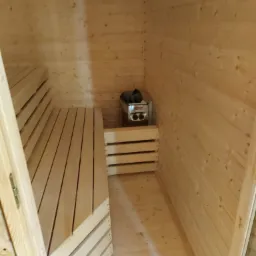 Wnętrze sauny wykończone jasnym drewnem, z ławkami i piecem elektrycznym marki Harvia.